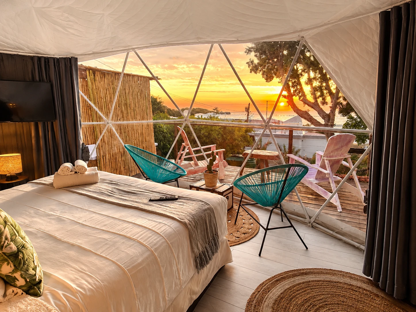 Panoramic interior of a glamping dome looking across a deck towards the ocean at sunset